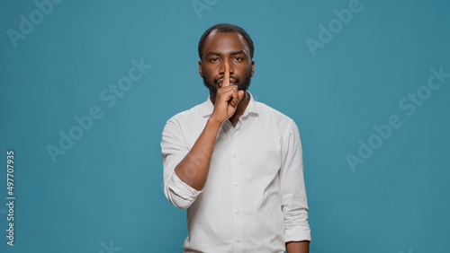Portrait of male model showing silence sign in front of camera, putting index finger over mouth to keep secret. Person advertising hush and mute gesture, privacy and confidential information.