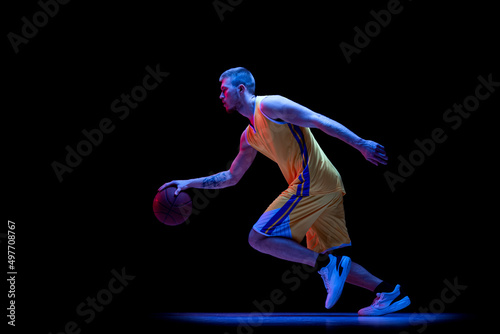 Dribbling. One sportive man, professional basketball player playing basketball isolated on dark background in neon light. Achievements, sport career, motion concepts.