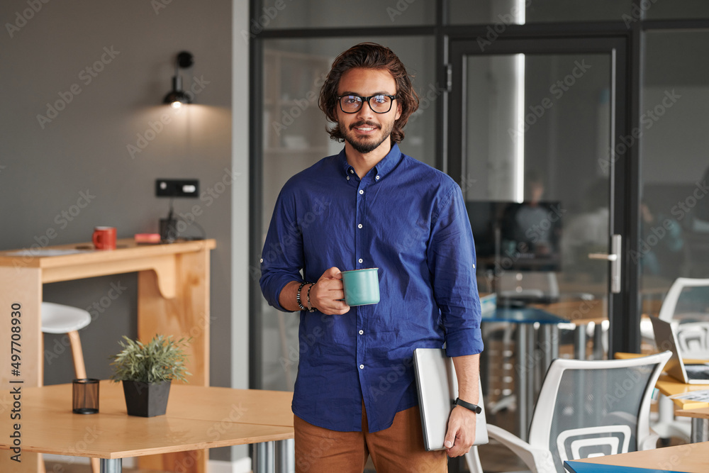 Fototapeta premium Portrait of smiling young mixed race app developer holding laptop and drinking coffee in coworking space
