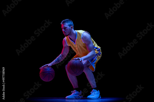 Dribbling. One sportive man, professional basketball player playing basketball isolated on dark background in neon light. Achievements, sport career, motion concepts.