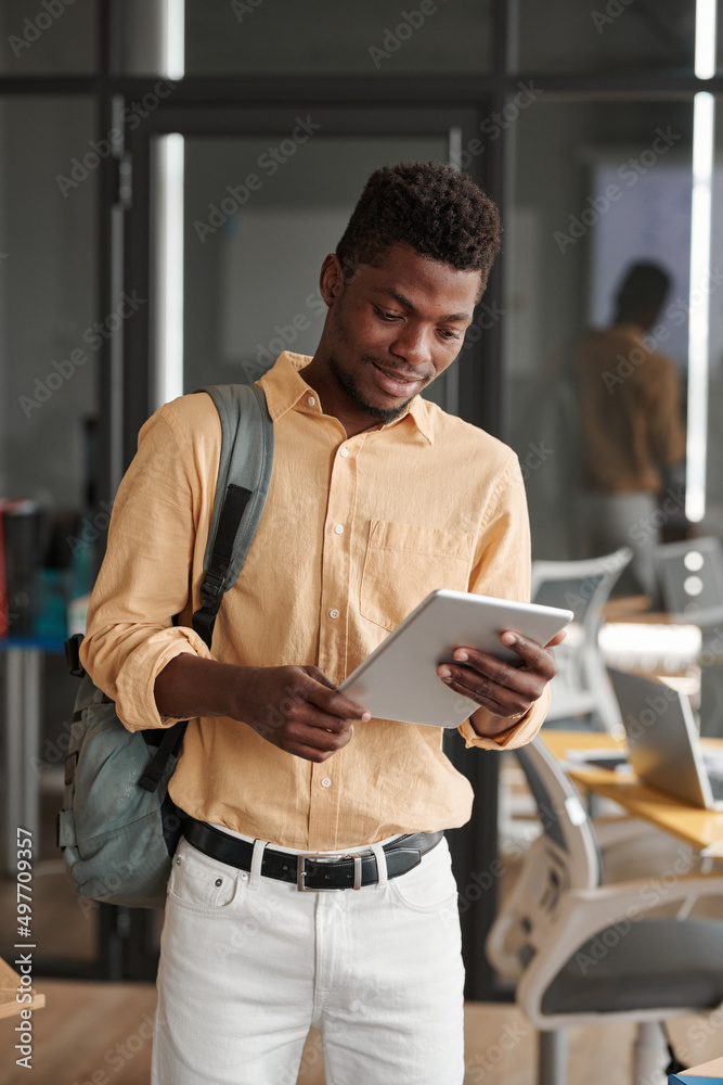 © Mediaphotos - Smiling young Black guy with satchel checking information on tablet in coworking space