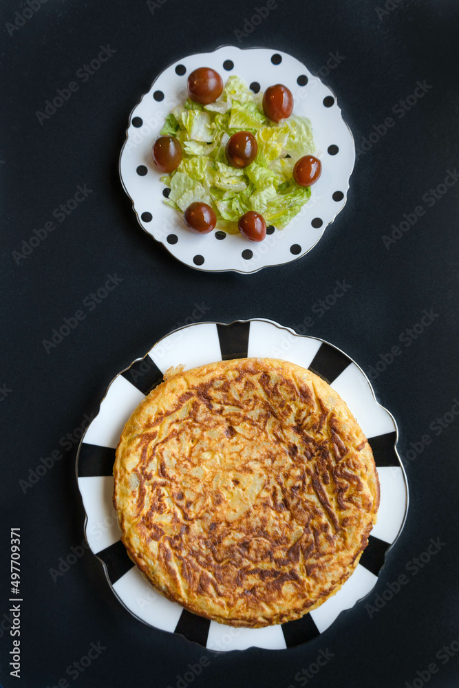 Two dishes, one Spanish omelette, and one green salad with roman lettuce, and cherry tomatoes with a black background Two dishes, one Spanish omelette, and one green salad with roman lettuce, and cherry tomatoes with a black background