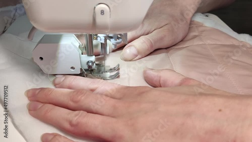 The process of sewing on a sewing machine. A stitch of pink fabric with insulation. A seamstress works on outerwear at home.