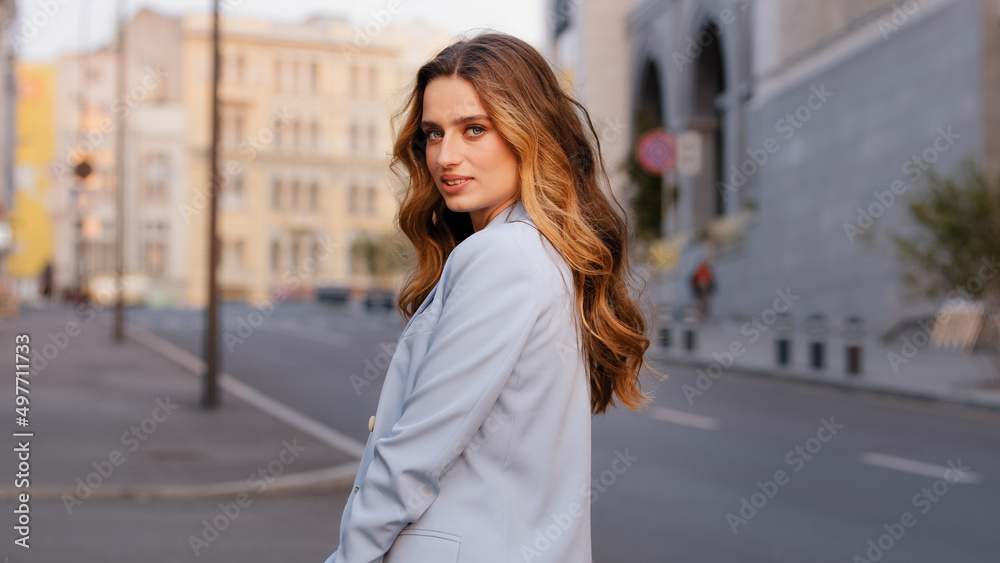 Young stylish caucasian attractive business woman manager in trendy blue suit posing in city looking at camera. Pretty carefree 20s lady girl model student standing in street outside outdoors