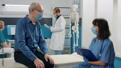 Elder person discussing about health care diagnosis with nurse  explaining disease treatment at checkup examination. Specialist having conversation with old man at appointment.