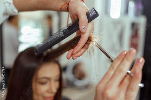 Close up of beautician hands holding a hair strand while cutting hair of woman. Hairstyling, beauty