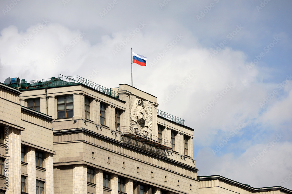 Russian flag on the parliament building in Moscow on background of blue sky and white clouds, authorities of Russia