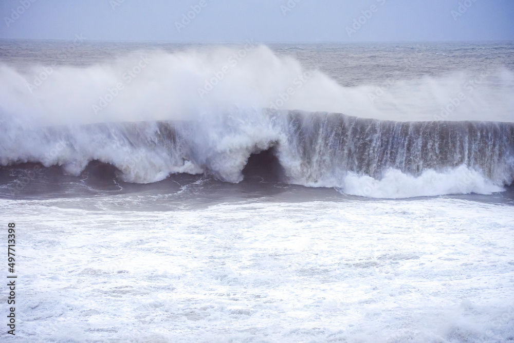 Big waves crashing on the sea with greenish blue color during a cloudy day