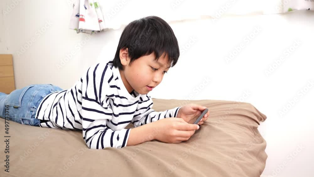 部屋でスマホを見ているアジア人の男の子