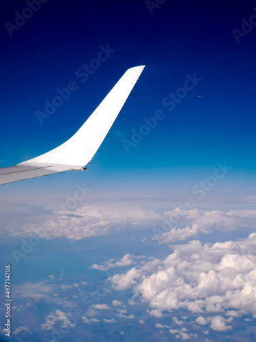 Aerial bright blue landscape from the aircraft with white wingtip. White Wing against blue sky and clouds