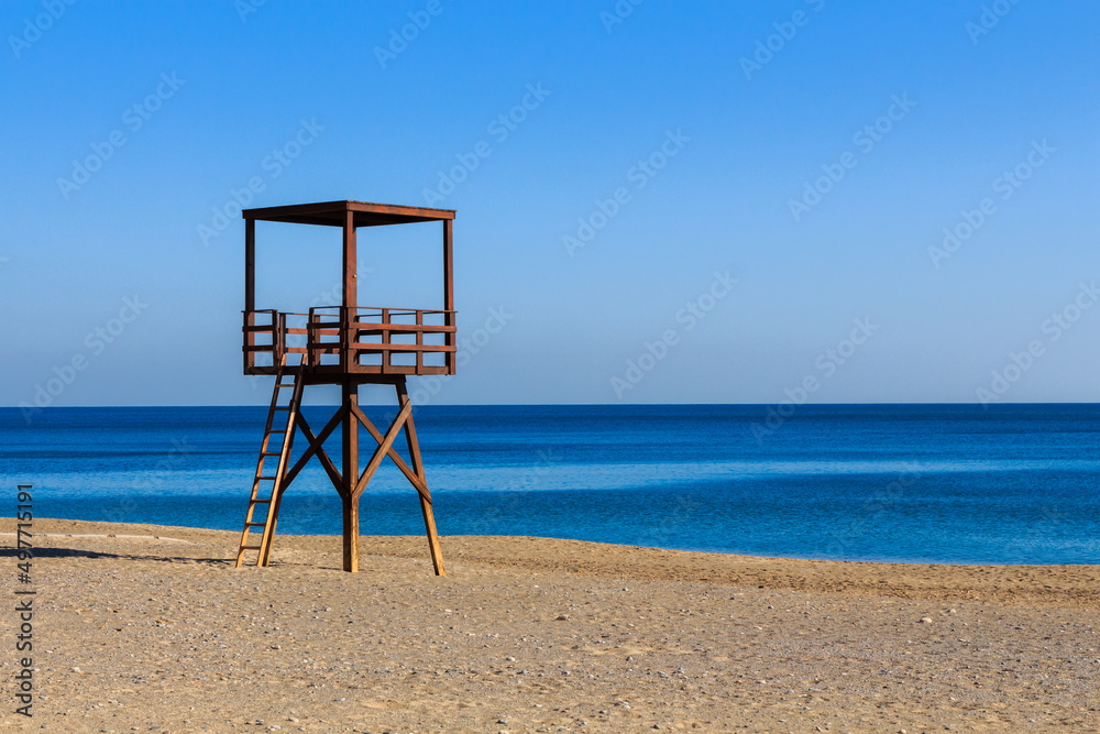 Wooden brown coastguard watchtower on the beach with blue sea in the background
