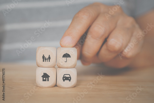 senior's hand holding umbrella icon on wooden cube block over family, vehicle and house symbol for health, property ,life, family, group insurance concept photo