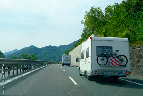 camper van with bicycle driving on the highway across blue sky and mountains peaks. Adventurous lifestyle. Camper life. Travel in mountains