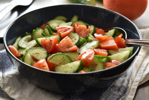 Cucumbers and tomatoes salad with herbs and salad dressing in a bowl.  Healthy and dietary food concept. 