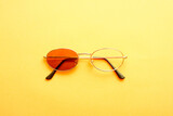 Sunglasses with one missing lens on yellow background.