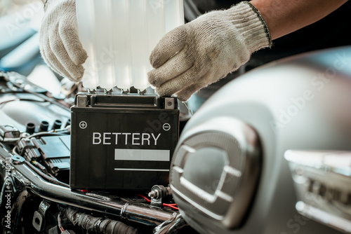 mechanic replaces motorcycle battery and holding Acid pack or sealed battery electrolyte pack to prepare for fill up battery,motorcycle maintenance and service and repair concept . selective focus photo