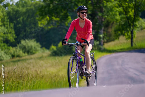 Closeup of smiling woman wearing bike helmet looking aside biking on a country road on a spring summer day. © Robert Peak