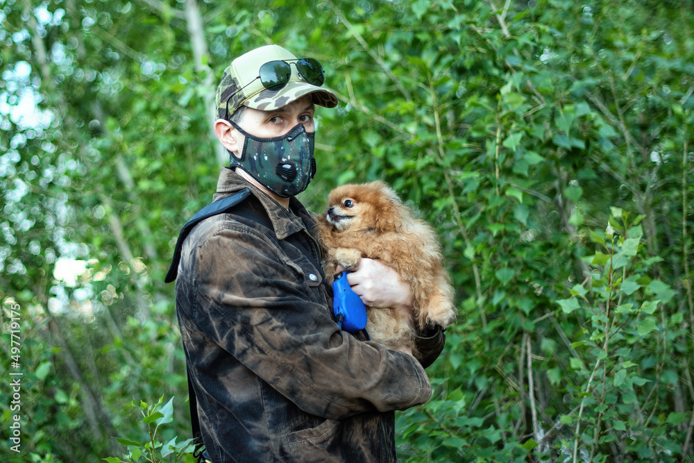 A man wearing respirator mask walking with a Pomeranian dog in the forest protecting from COVID-19.