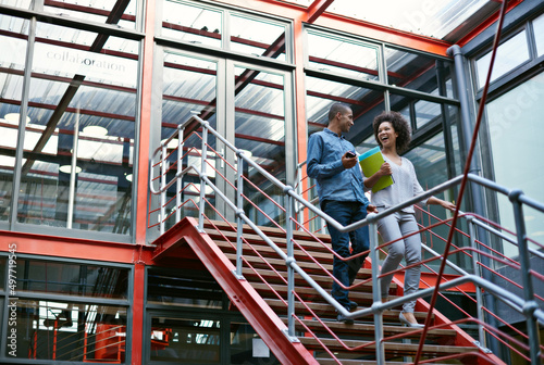 Communication is the key to success. Two colleagues walking side by side down stairs in their building. © Tabitha R/peopleimages.com