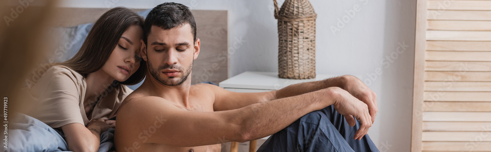 Muscular man sitting near girlfriend with closed eyes in bedroom, banner. Muscular man sitting near girlfriend with closed eyes in bedroom, banner.