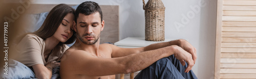 Muscular man sitting near girlfriend with closed eyes in bedroom, banner.