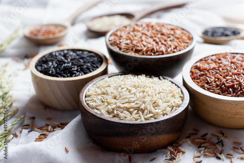Different types of rice grains put in a wooden cup placed on a white cloth, concept of food and health. © 994yellow
