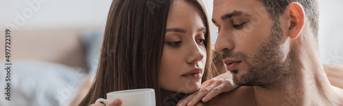 Pretty woman holding coffee near shitless man in bedroom, banner. photo