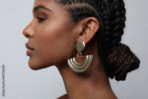 Close-up of African young woman with braids and earrings posing on grey wall.