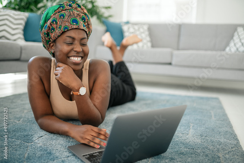 Black African woman laying on rug at home  legs crossed using laptop