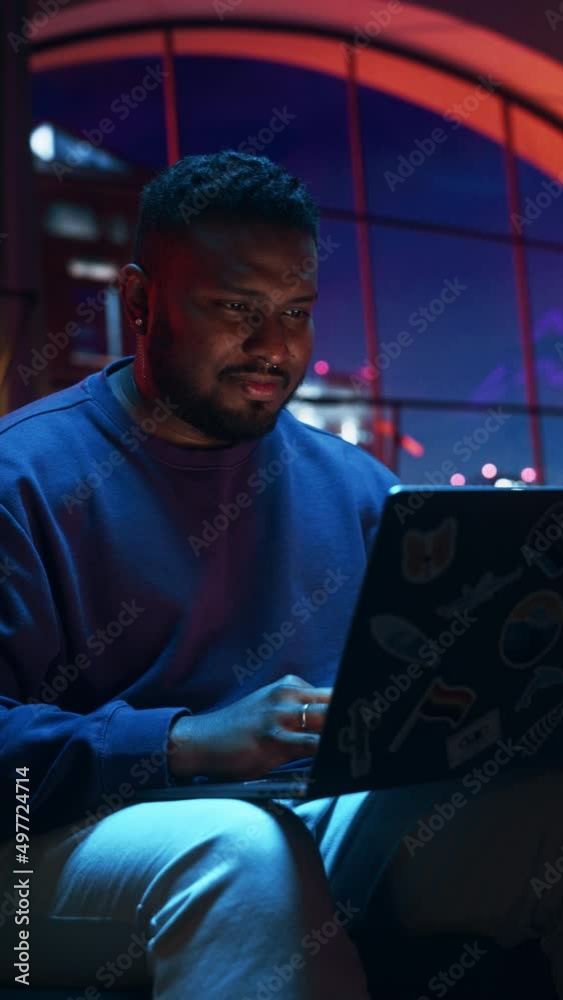Vertical Screen: Stylish Black Man Working from Home on Laptop Computer in Cozy Stylish Loft Apartment. Creative Male Smiling, Checking Social Media, Browsing Internet. Flat with Big Windows. Vertical Screen: Stylish Black Man Working from Home on Laptop Computer in Cozy Stylish Loft Apartment. Creative Male Smiling, Checking Social Media, Browsing Internet. Flat with Big Windows.