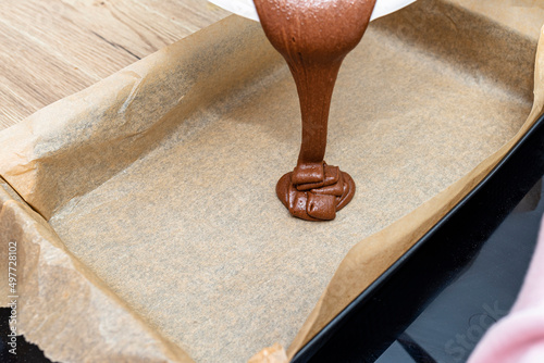 Obraz na plátně Pouring a liquid thick mass of cocoa dough onto a baking sheet lined with baking paper