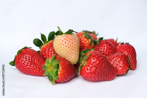 Ripe white pink strawberry on a pile of red strawberries isolated on white background
