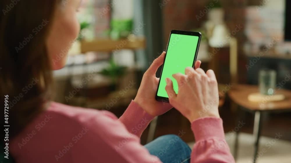 Feminine Hand Tapping on Display and Scrolling Feed on Smartphone with Green Screen Mock Up Display. Female Resting at Home, Checking Social Media on Mobile Device. Close Up Over the Shoulder Footage. Feminine Hand Tapping on Display and Scrolling Feed on Smartphone with Green Screen Mock Up Display. Female Resting at Home, Checking Social Media on Mobile Device. Close Up Over the Shoulder Footage.