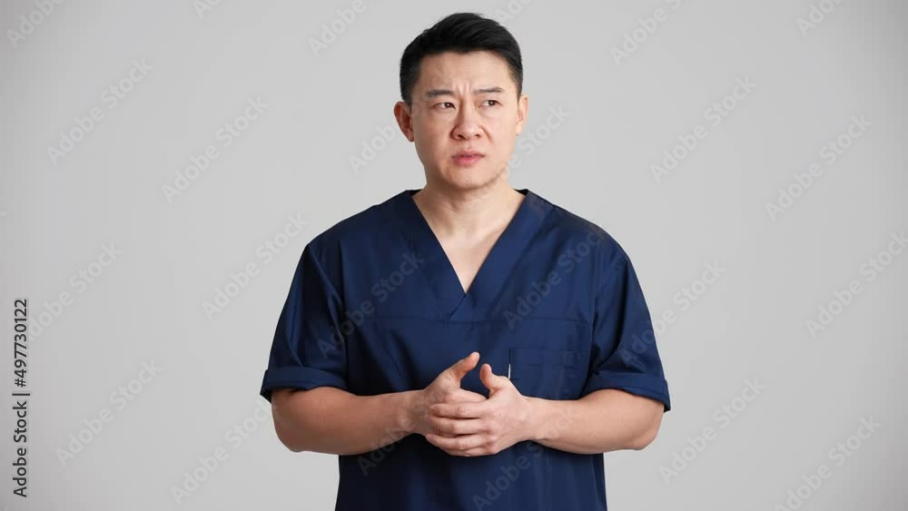 Sad Asian doctor talking something at the camera in the grey studio