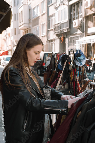 A young girl chooses an eco-friendly lifestyle and buys clothes at second hand stores. A European girl with long dark hair chooses a jacket in a vintage store on the street.