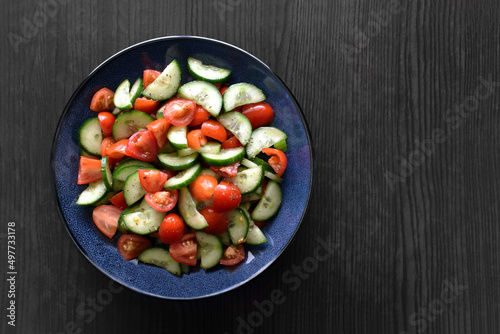 Cucumbers and tomatoes salad with herbs and salad dressing in a bowl. Healthy and dietary food concept. Flat lay food photo.