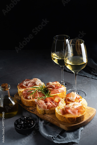 Italian appetiser - bruschetta with prosciutto, white wine, rosemary branch, olive oil and black olives