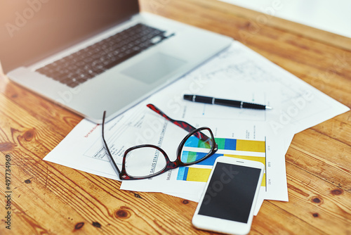 The modern businessmans essentials. Cropped shot of a laptop, smartphone, glasses and paperwork on a desk.