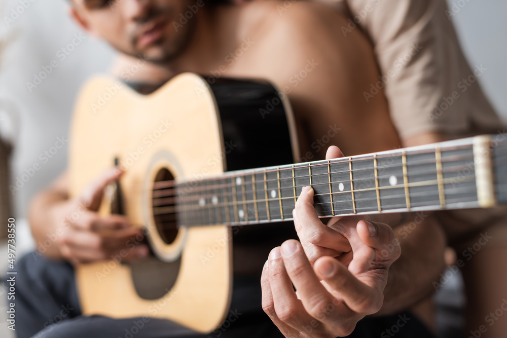 Cropped view of blurred couple playing acoustic guitar at home.