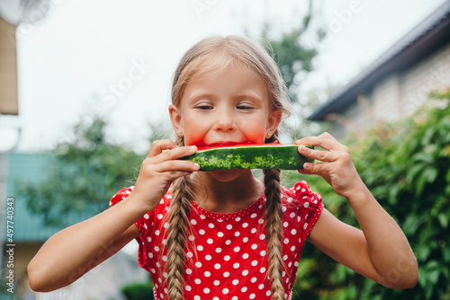 Little girl in red dress eating watermelon in the garden.