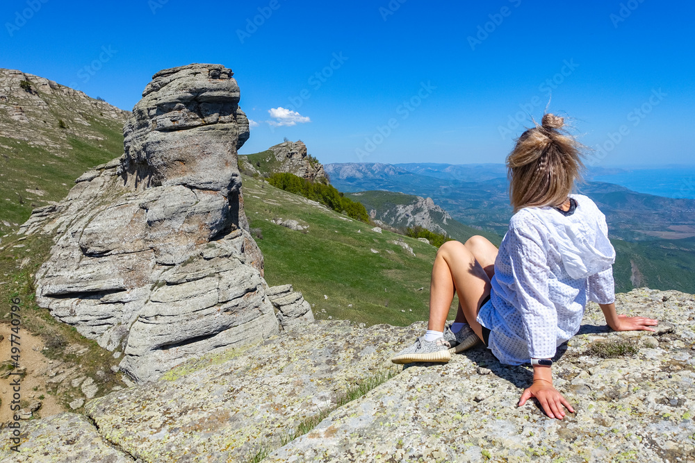 Naklejka premium A girl on the background of a view of the Black Sea and the stone conglomerates of the Demerdzhi ridge. May.