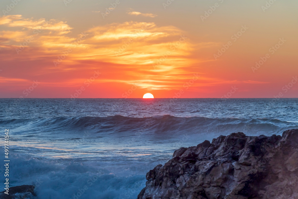 Sunset at Atlantic ocean coast with cliffs, rock formations and a dramatic sky over the white strong waves, Portugal