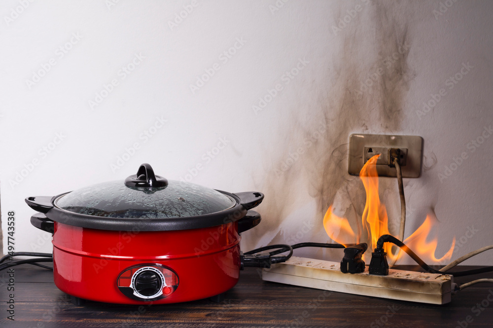 Cooking with an electric pan causes a short circuit. The power plug  contains flames and smoke. Fire ignites. Using non-standard equipment is  dangerous. overload Stock Photo