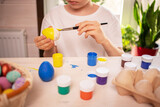 boy in a white t-shirt paints eggs to celebrate the Easter holiday with bright colors. Childish art, handmade culture concept. Boy with a brush in his hand paints an egg.