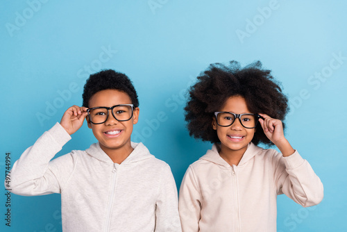 Portrait of attractive cheerful intellectual friends schoolkids nerds touching specs isolated over bright blue color background