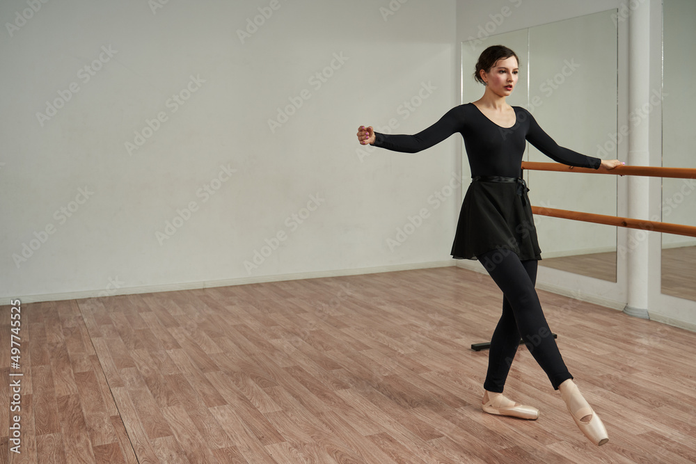 a ballerina in a dance class holds her hand on a ballet barre and gracefully stretches her leg forward. dance practice. a ballerina in a dance class holds her hand on a ballet barre and gracefully stretches her leg forward. dance practice.