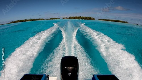 View over the outboard engines of a speedboat flying over the tropical blue lagoon of Fakarava, French Polynesia. Camera tilts up into the blue sky photo