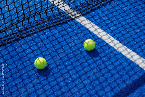 two paddle tennis balls in the shade of the net of a blue paddle tennis court © Vic