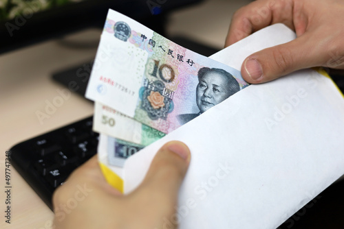Envelope with Chinese yuan in male hands. Man pulls money out of an envelope on PC keyboard background, wages, bonus or bribe concept photo