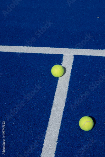 two paddle tennis balls next to the lines of a blue paddle tennis court © Vic